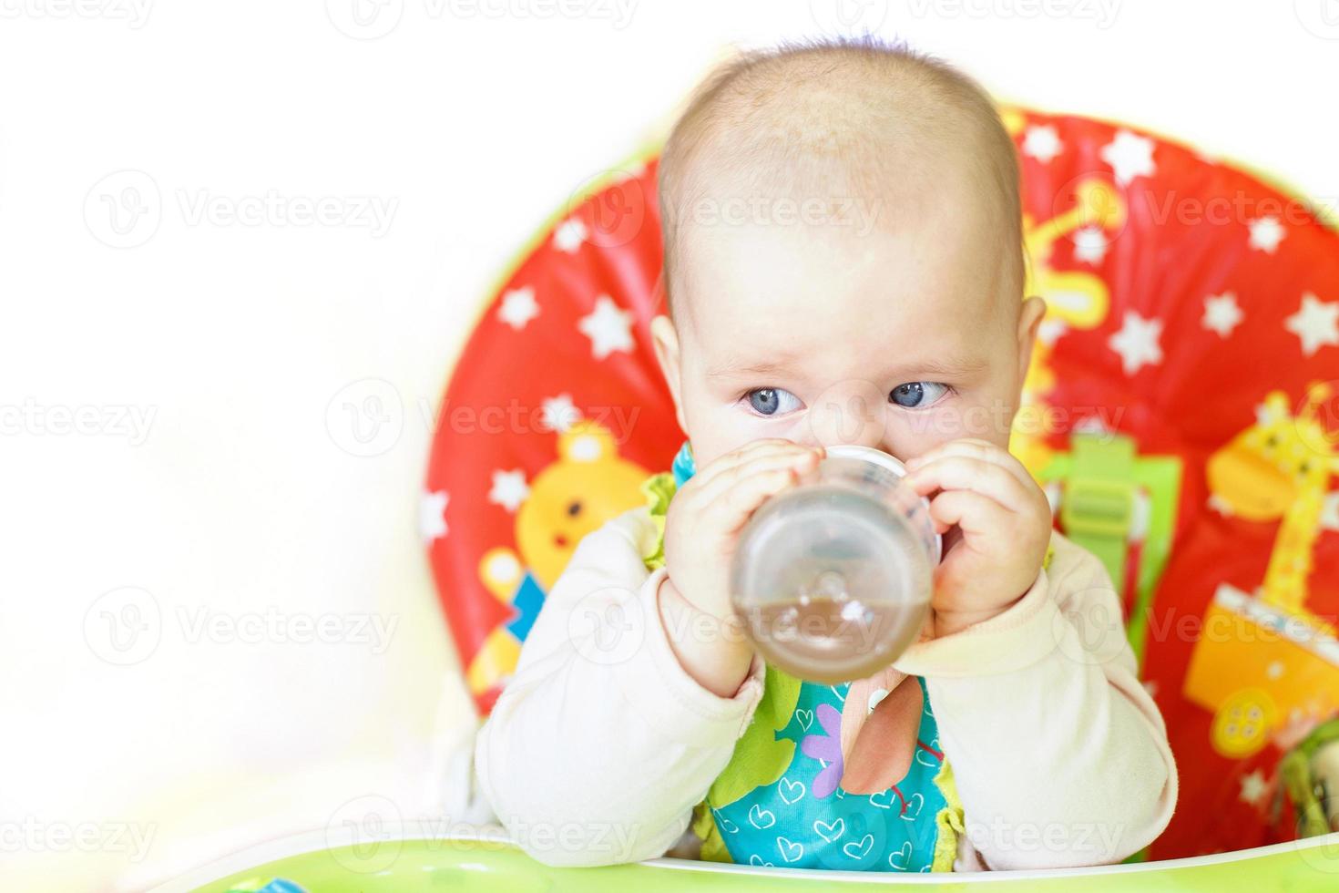 Baby trinken aus der Flasche sitzen im Hochstuhl auf weißem Hintergrund foto