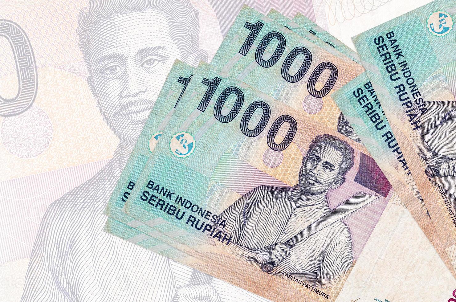 1000 indonesische Rupiah-Scheine liegen im Stapel auf dem Hintergrund einer großen halbtransparenten Banknote. abstrakte Darstellung der Landeswährung foto