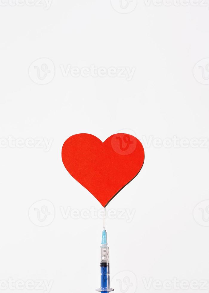 sicheres impfkonzept mit platz für text oben. Spritze mit Impfstoff und einem großen roten Herzen auf weißem Hintergrund, Draufsicht. vertikale Perspektive foto