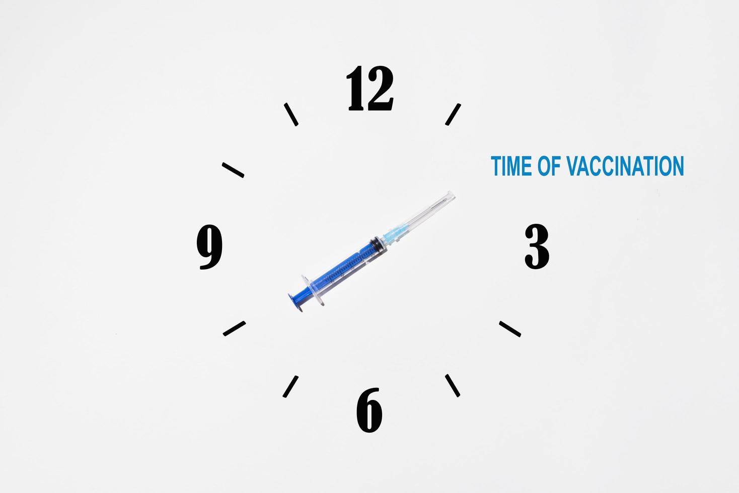 kreatives Konzept der Impfung der Weltbevölkerung. Spritze mit Angabe der Impfzeit auf dem Ziffernblatt der Uhr foto