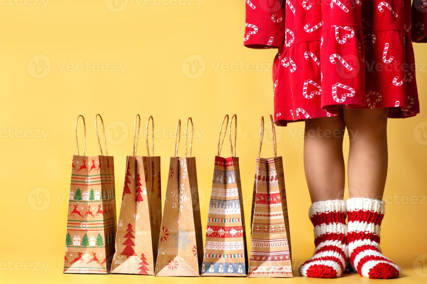 lieferung weihnachtsgeschenke einkaufen handwerk papiertüten geschenke und kind in gestrickten socken isoliert gelber hintergrund foto