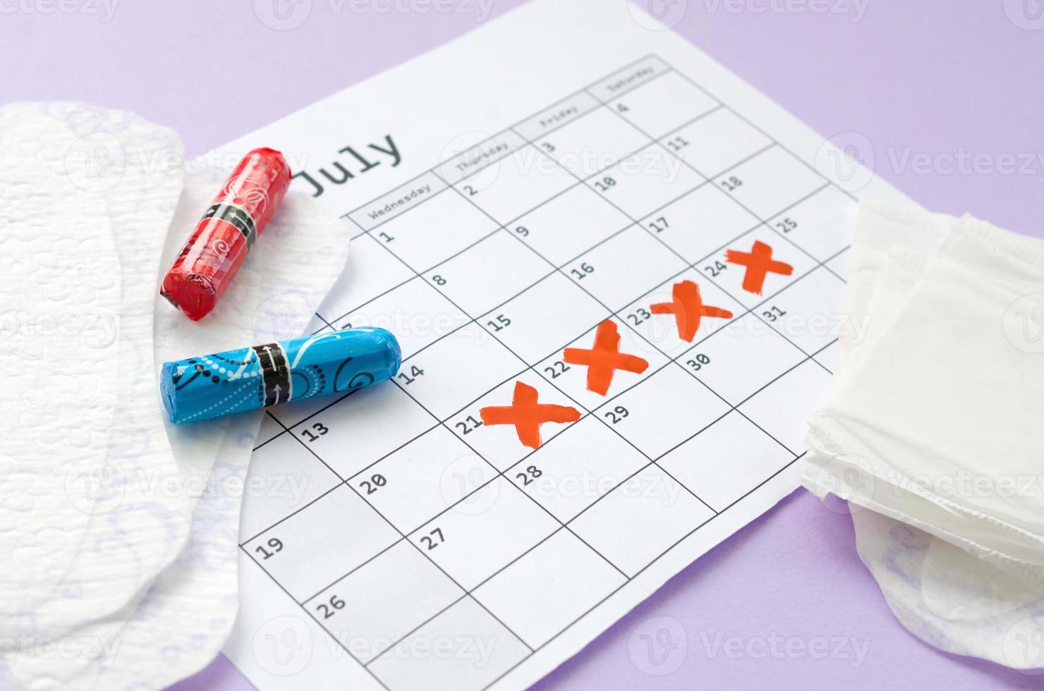 menstruationspads und tampons auf dem menstruationsperiodenkalender mit roten kreuzmarkierungen liegen auf fliederhintergrund foto