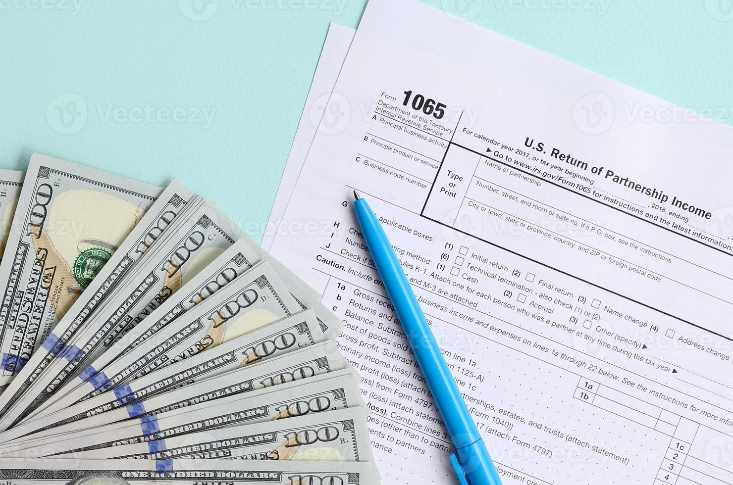 1065 Steuerformular liegt in der Nähe von Hundert-Dollar-Scheinen und blauem Stift auf hellblauem Hintergrund. uns für Elternschaftseinkommen zurückgeben foto