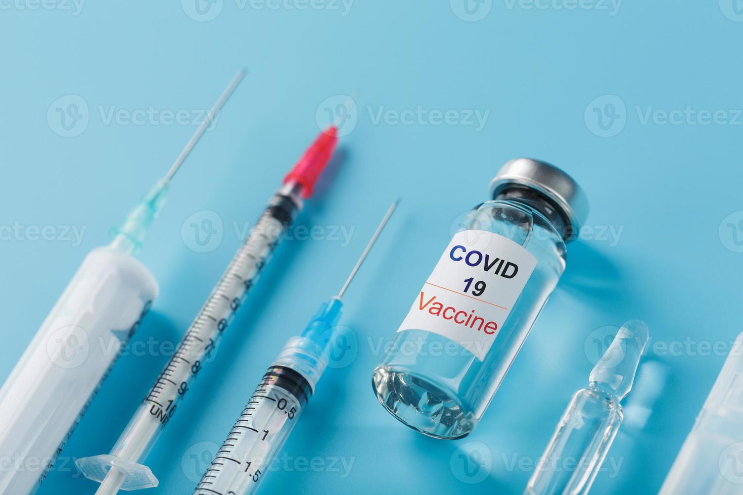 ein satz ampullen mit der aufschrift covid-19 impfstoff und ein satz spritzen vor blauem hintergrund. foto