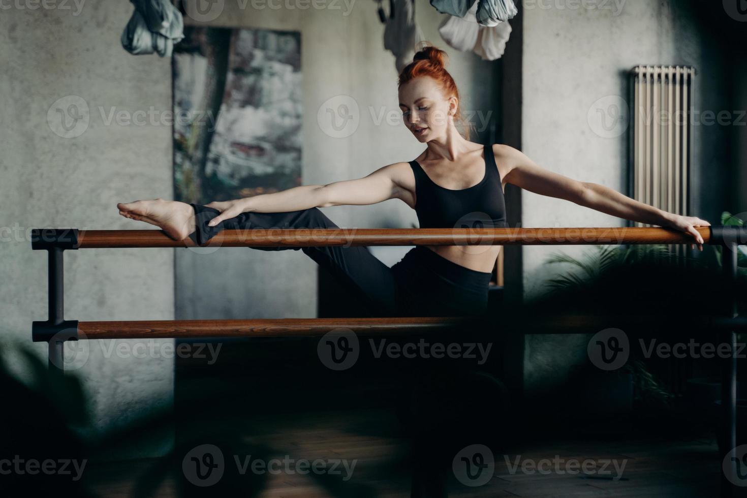 Junge rothaarige Frau in guter Körperform, die Dehnübungen auf der Ballettstange macht foto