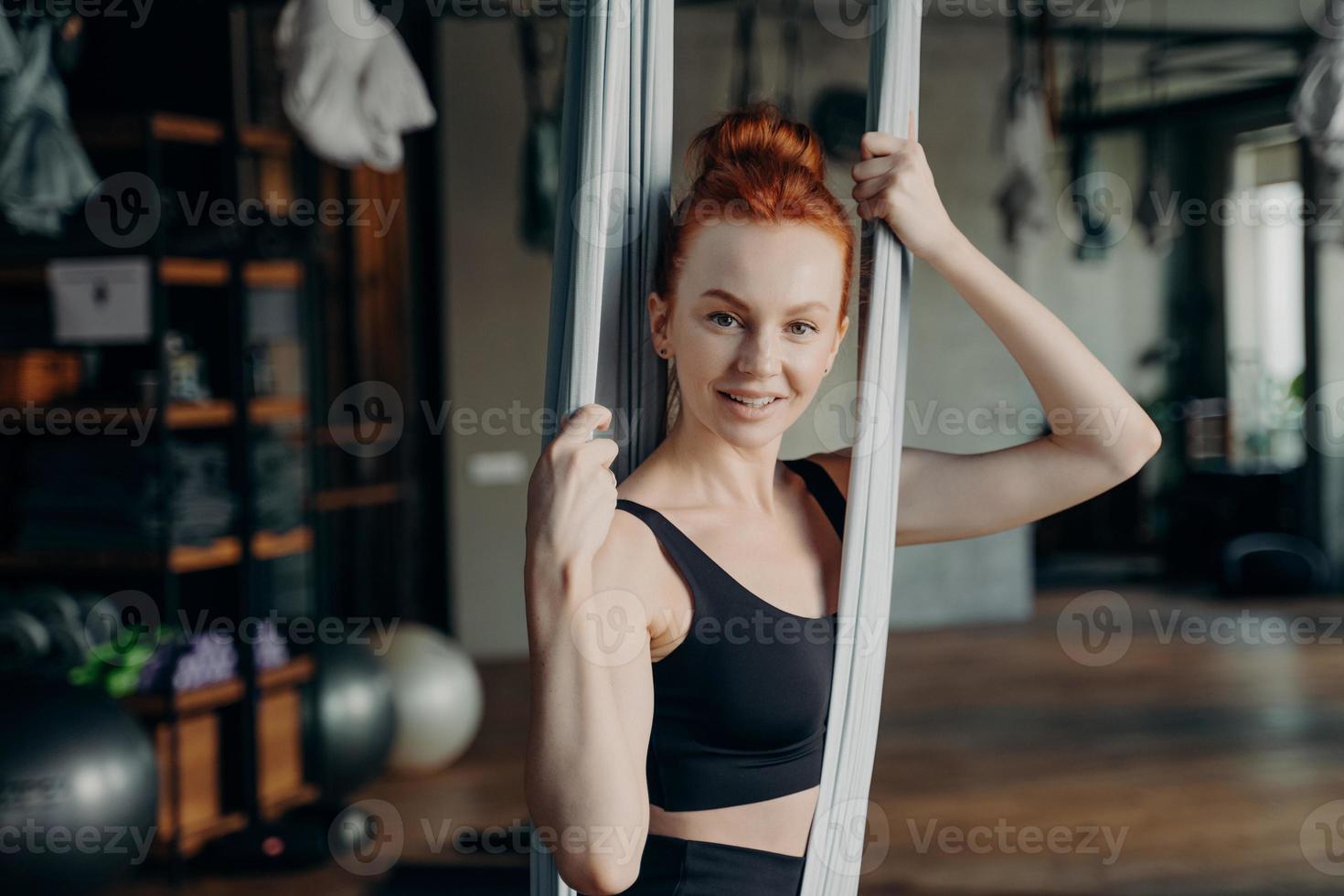 Junge aktive Frau im Trainingsanzug, die auf einer Yoga-Hängematte sitzt foto