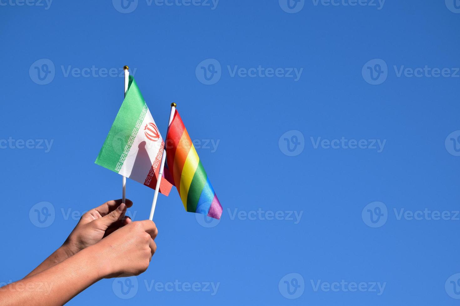 iranische flagge und regenbogenflagge, lgbt-symbol, in händen halten, blauer hintergrund, konzept für lgbt-feier im iran und auf der ganzen welt im stolzmonat, juni, weicher und selektiver fokus, kopierraum. foto