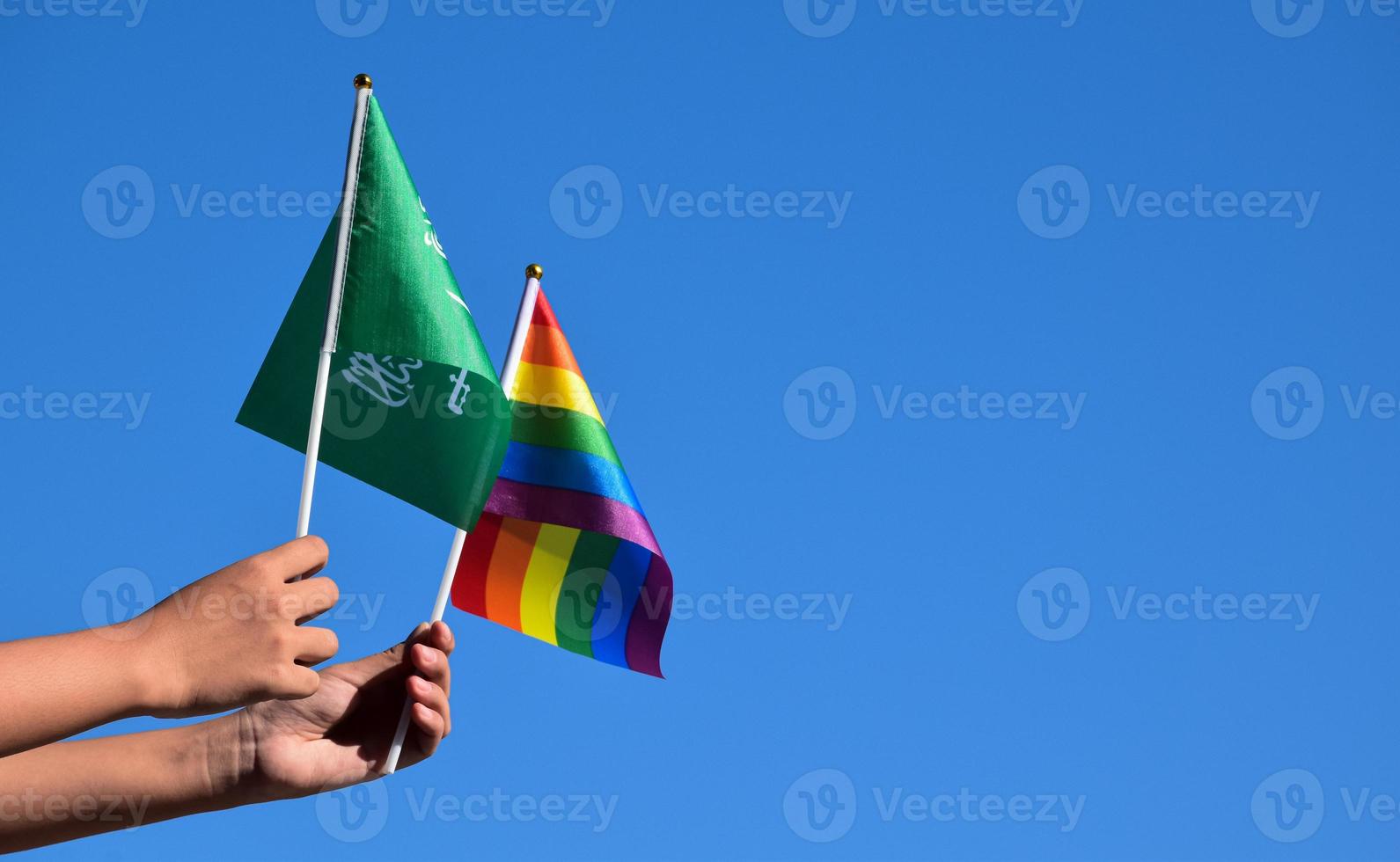 saudi-arabien-flagge und regenbogenfahne, lgbt-symbol, in händen halten, blauer himmelshintergrund, konzept für lgbt-feier in saudi-arabien im stolzmonat, juni, weicher und selektiver fokus. foto