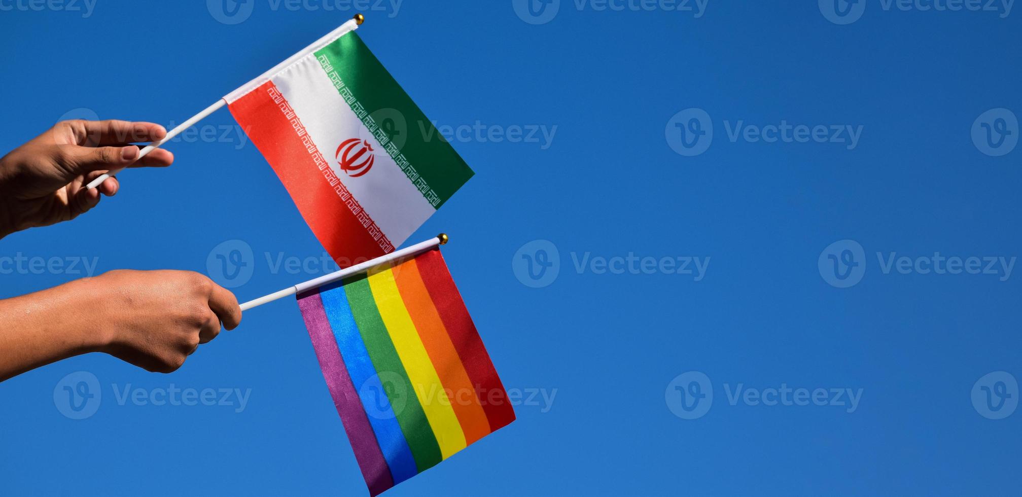 iranische flagge und regenbogenflagge, lgbt-symbol, in händen halten, blauer hintergrund, konzept für lgbt-feier im iran und auf der ganzen welt im stolzmonat, juni, weicher und selektiver fokus, kopierraum. foto