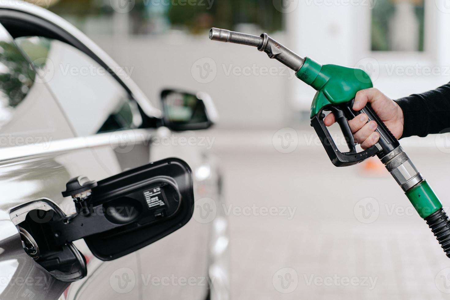 beschnittene Aufnahme der Hand des Mannes, die an der Tankstelle Benzin in das Auto pumpt. Auto wird mit Benzin gefüllt. nicht erkennbarer mann hält tankdüse. foto