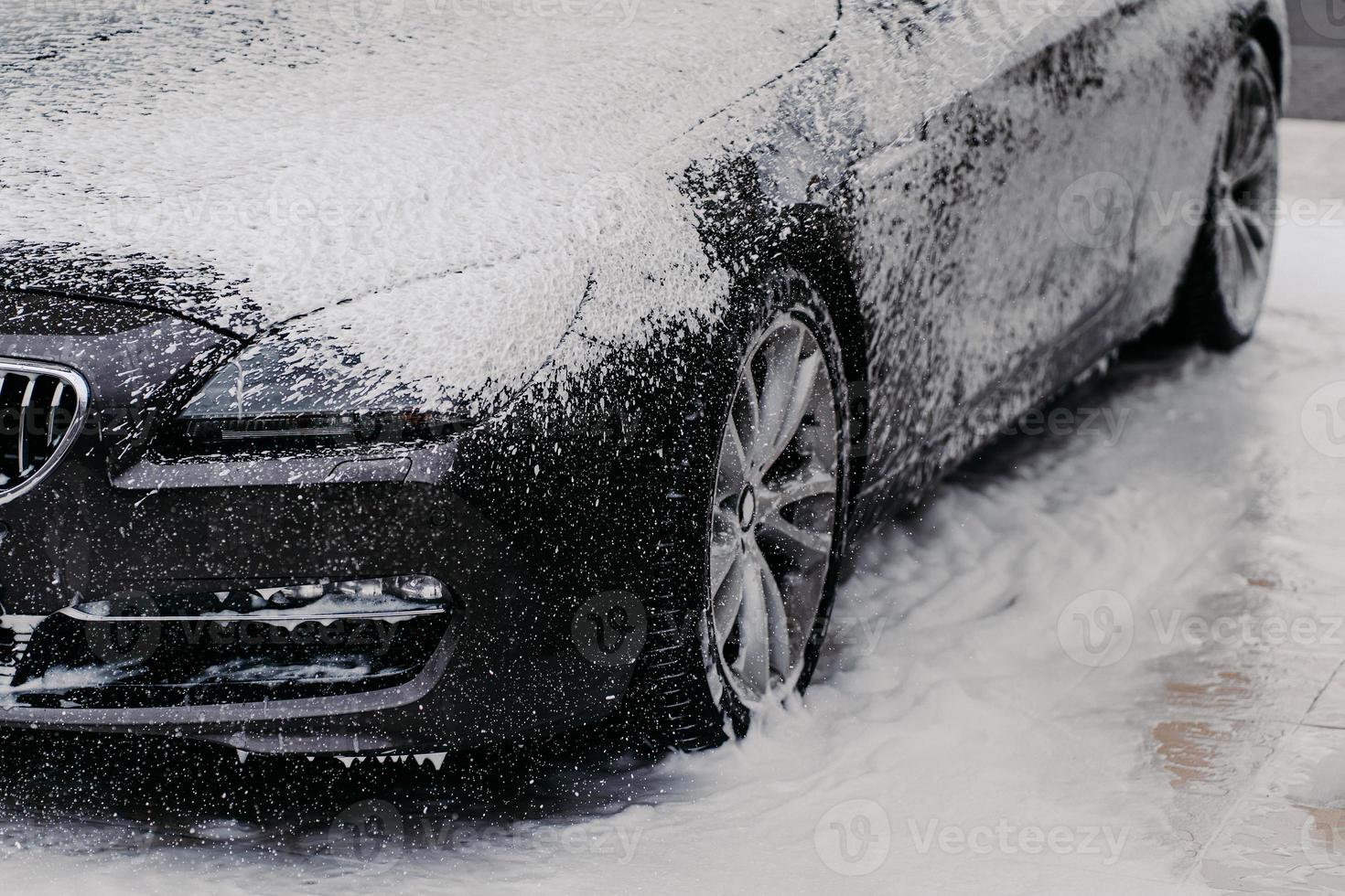 horizontale Aufnahme eines schwarzen Automobils, das bei der Autowäsche mit Schaumseife bedeckt ist. Detailreinigung. Reinigungskonzept foto