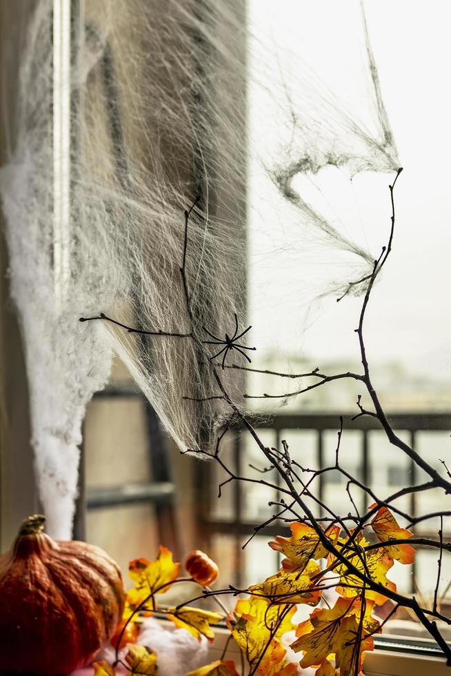 halloween-konzept, dekoriertes fenster mit spinnweben, herbstgelben blättern, kahlen baumasten und einem kürbis auf dunklem hintergrund foto