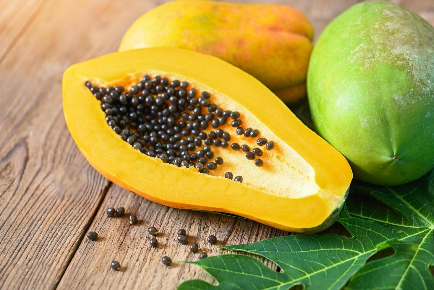 frische reife Papaya-Tropenfrucht mit Papaya-Samen und Blattblättern vom Papaya-Baum, Papaya-Früchte auf Holzhintergrund foto