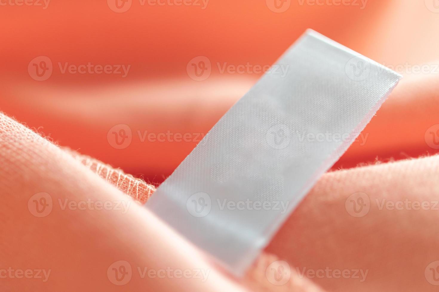 leeres weißes etikett für wäschepflegekleidung auf rosa stoffstrukturhintergrund foto