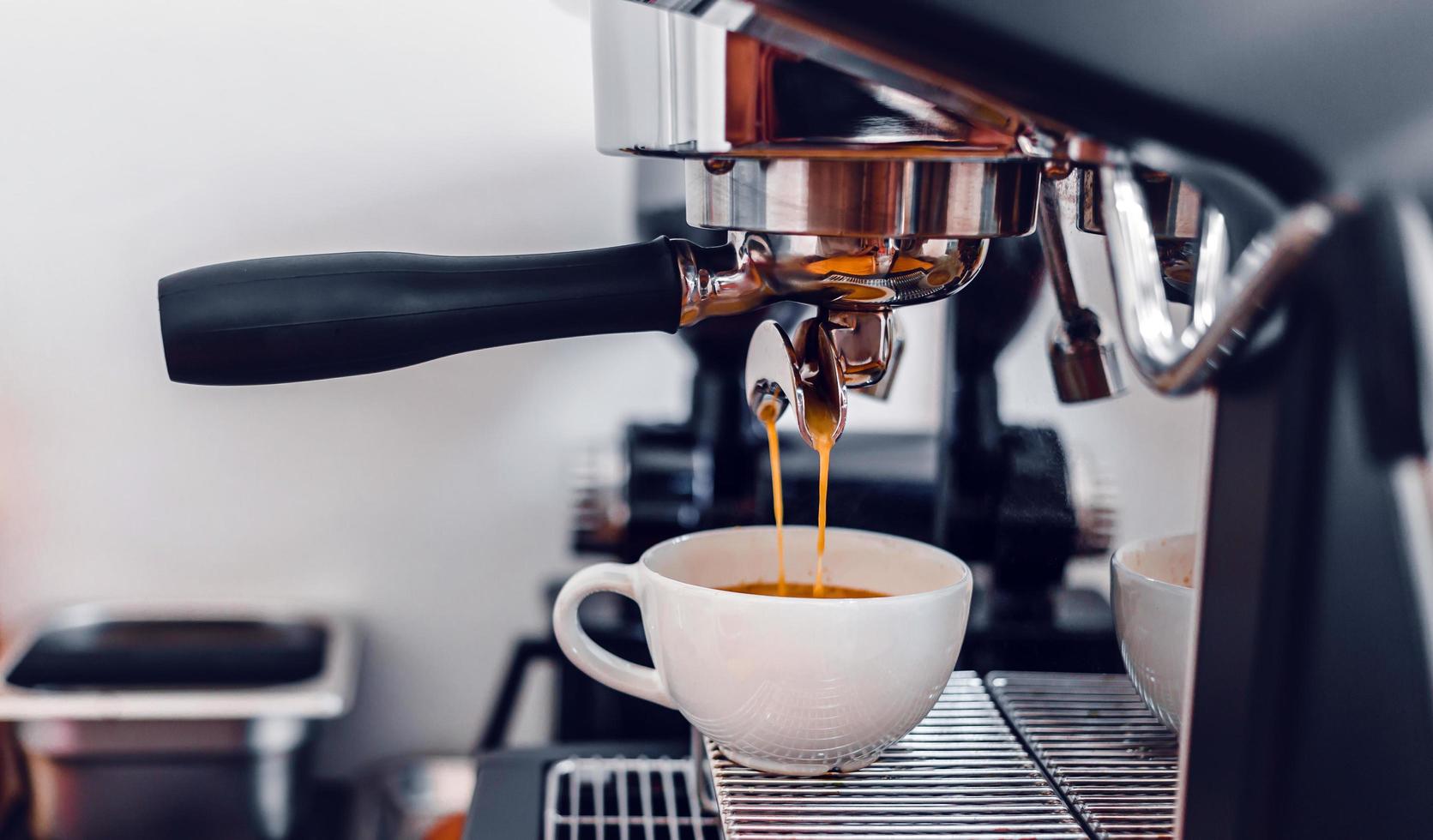 Kaffeeextraktion aus der Kaffeemaschine mit einem Siebträger, der Kaffee in eine Tasse gießt, Espresso aus der Kaffeemaschine im Café foto
