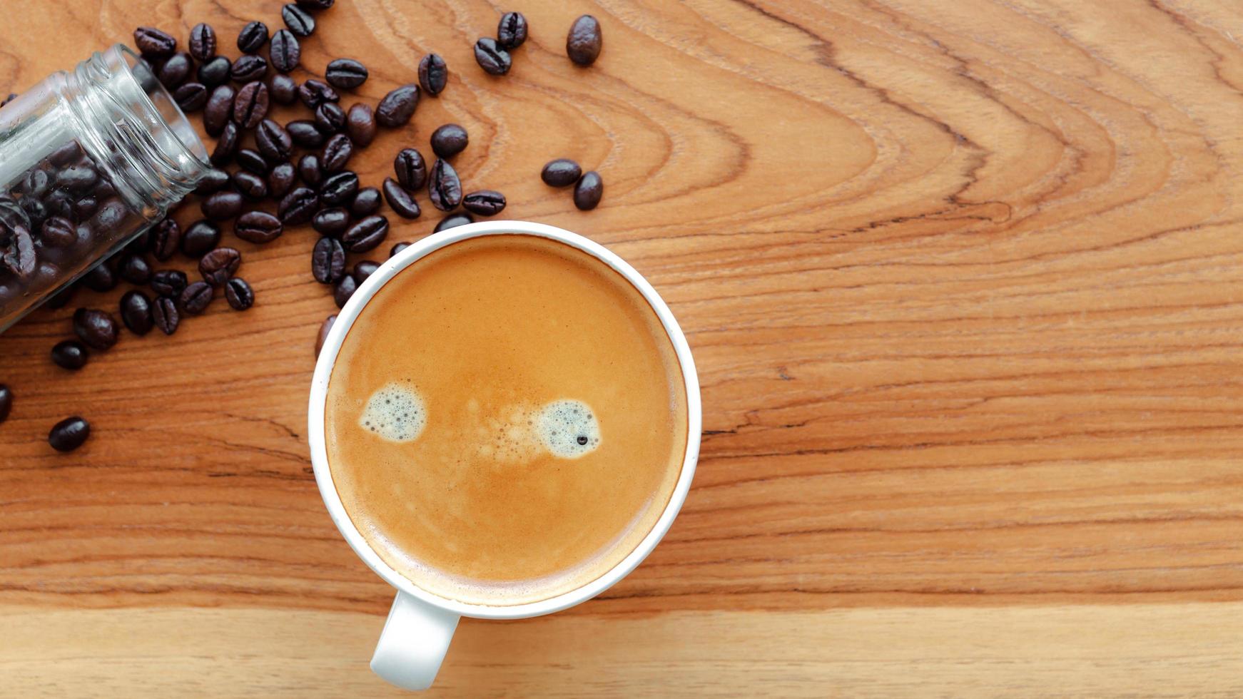 Weiße Tasse Espressokaffee und geröstete Kaffeebohnen auf Holzhintergrund foto