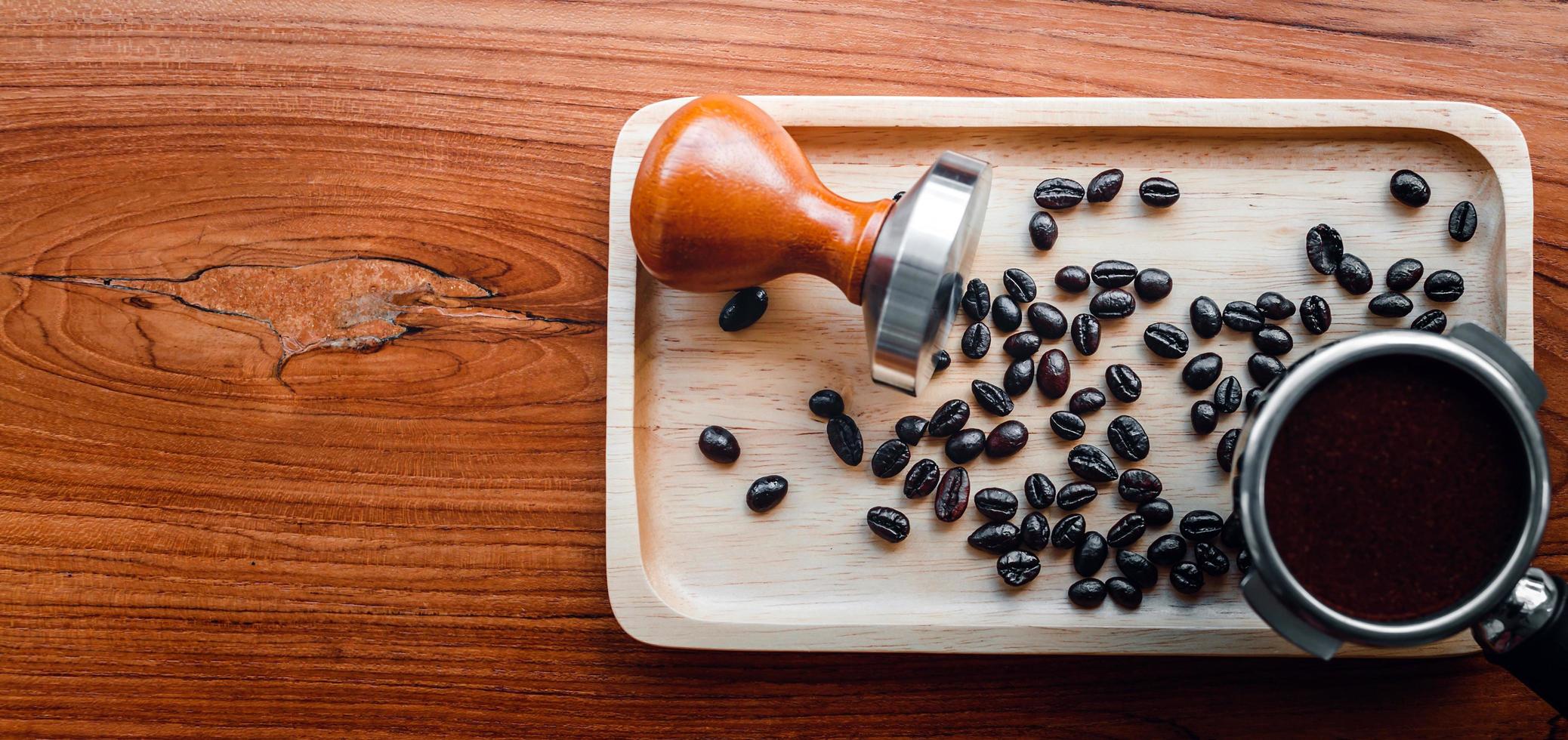 Ausrüstung von Barista Coffee Tool Tamper und temperierter Kaffee in Portafilter geröstete Kaffeebohnen auf Holztisch foto