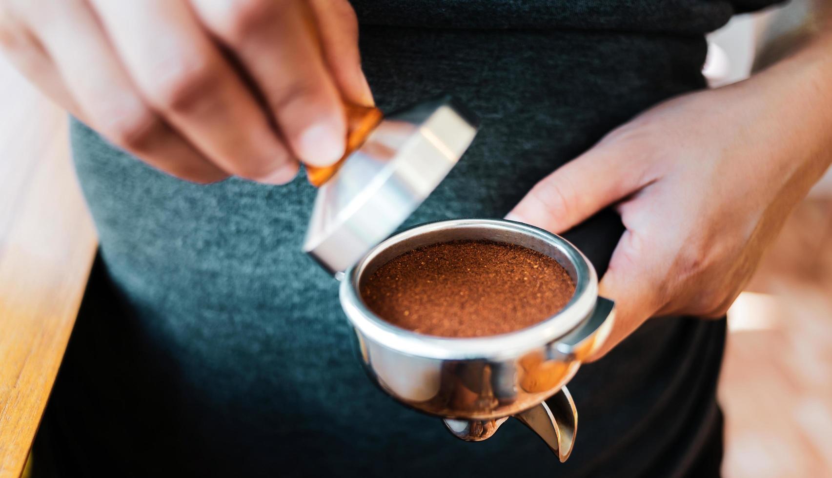 Nahaufnahme des Hand-Barista-Cafés, das Kaffee mit manuellen Pressen gemahlenen Kaffee mit Tamper im Café zubereitet foto