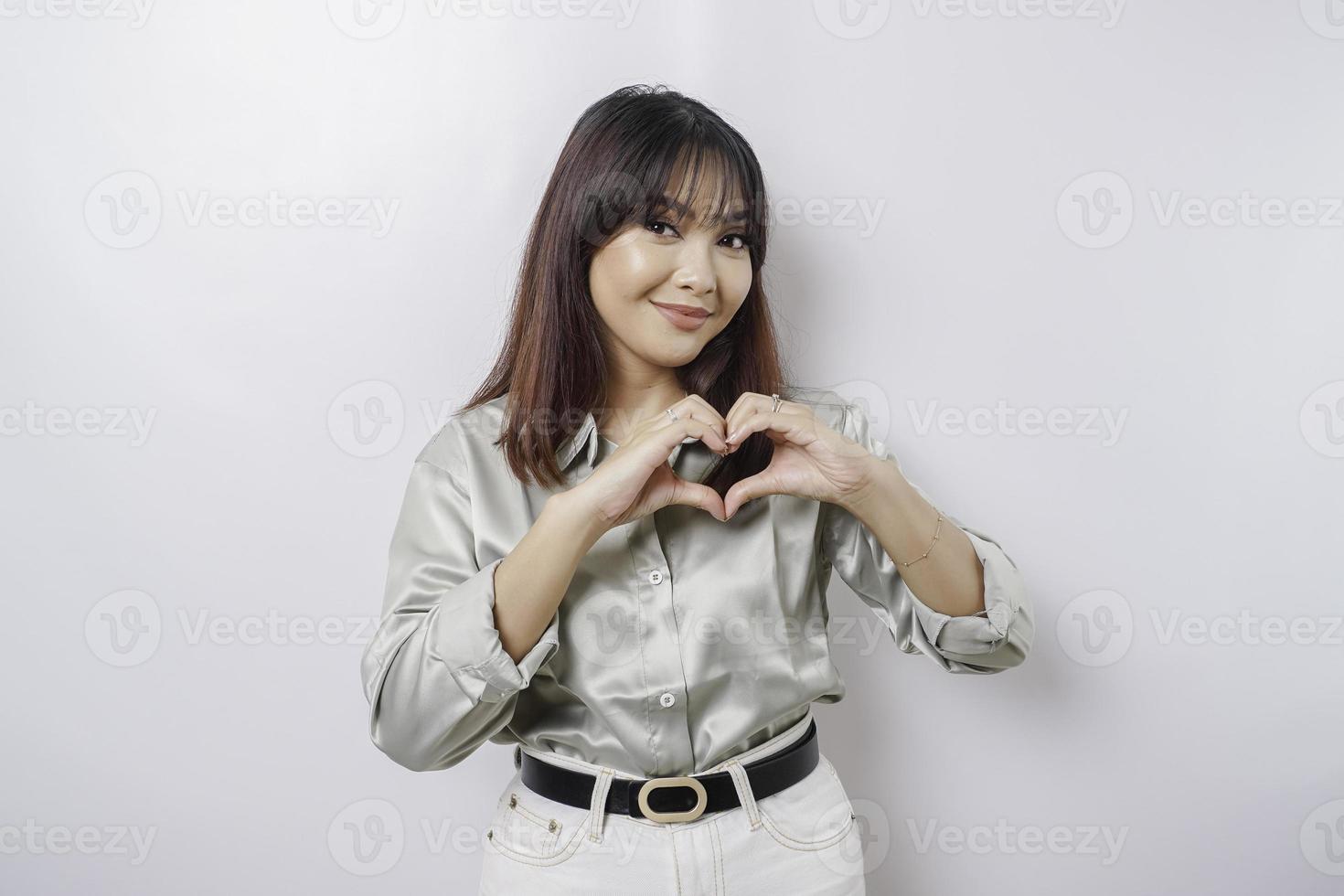 eine attraktive junge asiatische frau, die ein salbeigrünes hemd trägt, fühlt sich glücklich und eine romantische formherzgeste drückt zärtliche gefühle aus foto