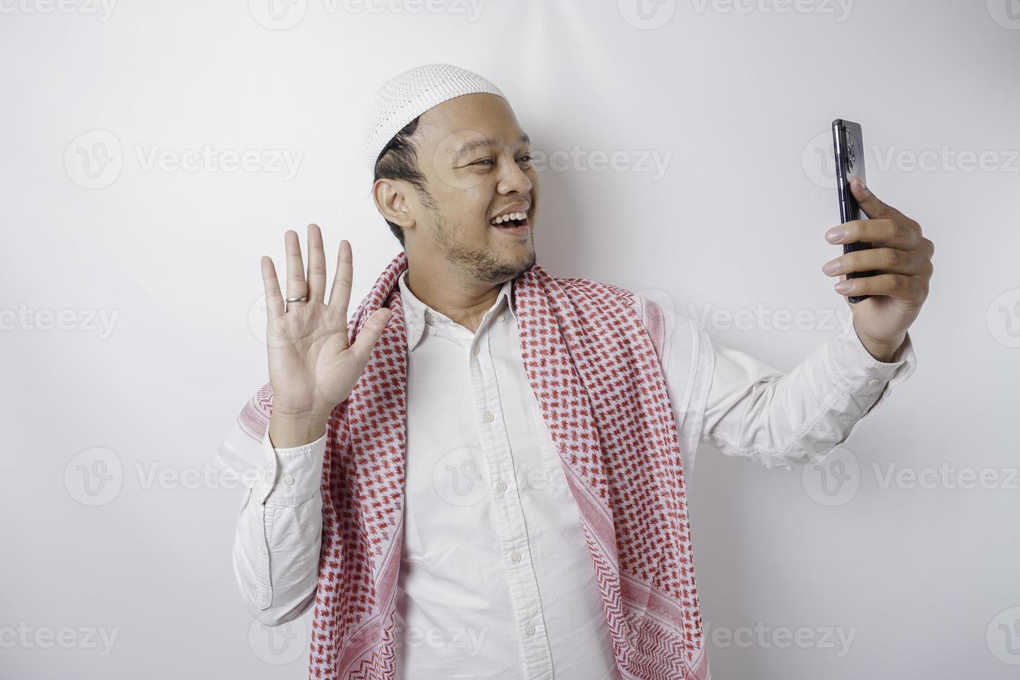 ein Porträt eines glücklichen asiatischen muslimischen Mannes, der lächelt, während er sein Telefon hält, isoliert durch weißen Hintergrund foto