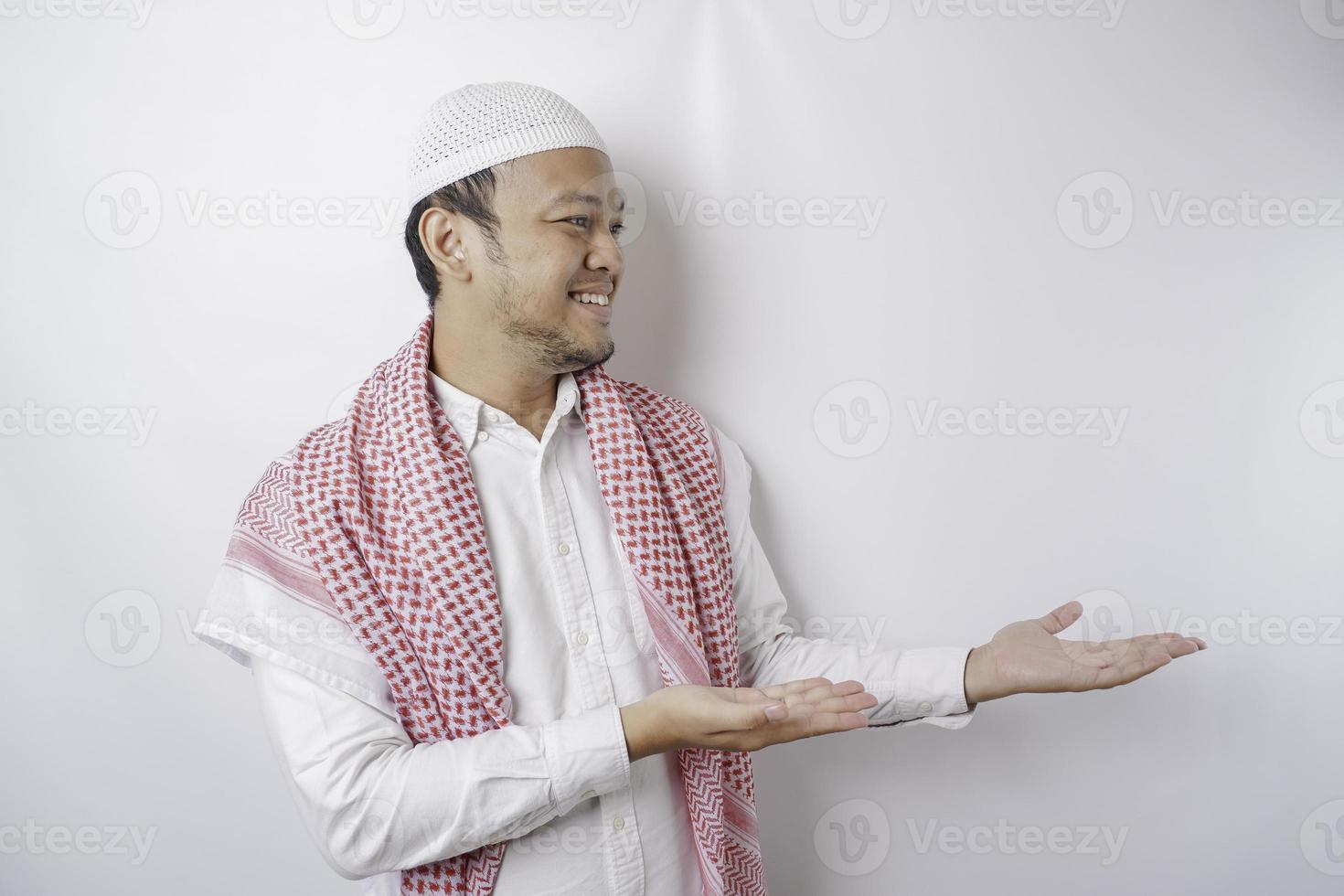 Aufgeregter asiatischer muslimischer Mann, der auf den Kopierbereich neben ihm zeigt, isoliert durch weißen Hintergrund foto