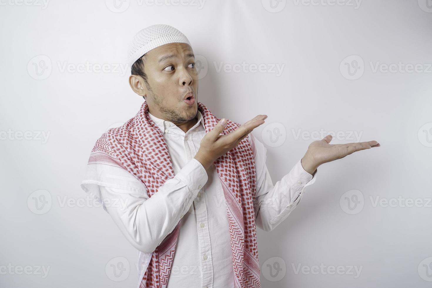 schockierter asiatischer muslimischer mann, der auf den kopierraum neben ihm zeigt, isoliert durch weißen hintergrund foto
