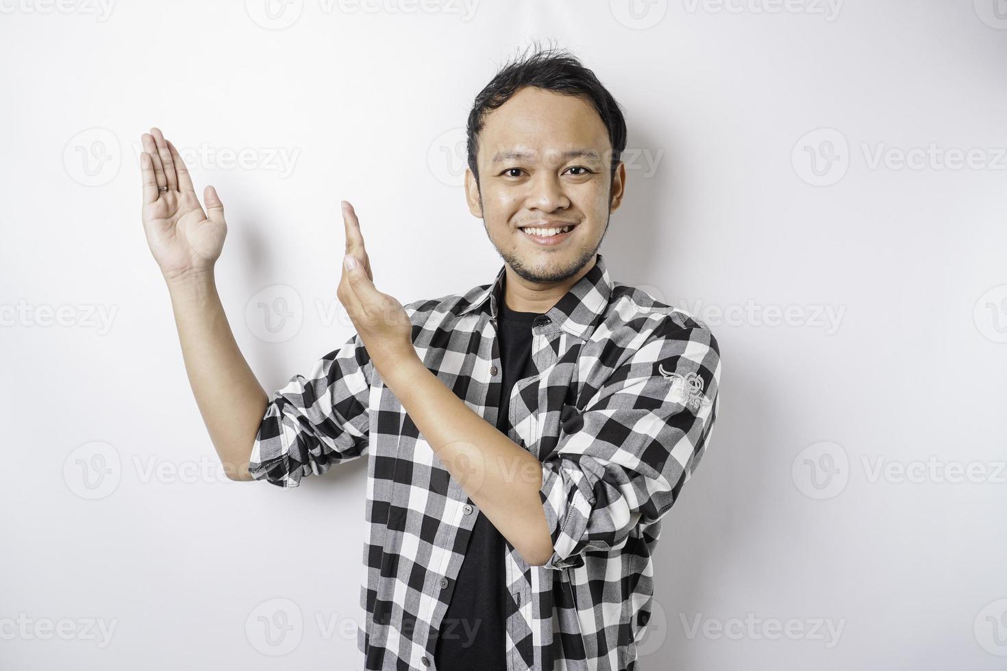 Der lächelnde asiatische Mann mit Tartanhemd zeigt auf den Kopierbereich auf ihm, isoliert durch weißen Hintergrund foto