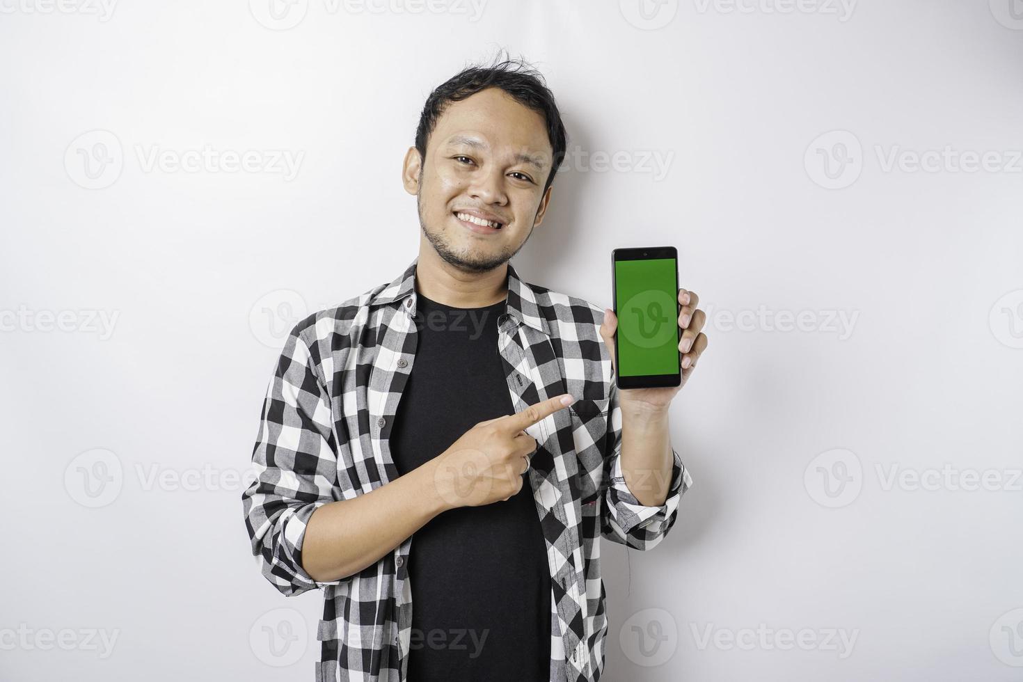 Ein Porträt eines glücklichen asiatischen Mannes lächelt, während er auf seinem Telefon Platz für Kopien zeigt, isoliert durch weißen Hintergrund foto