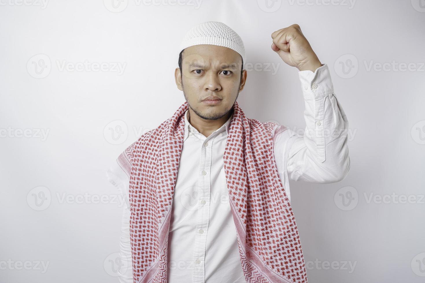 junger asiatischer muslimischer mann, der sich ernst fühlt und konzentriert auf die kamera starrt, während er seine hand hebt foto