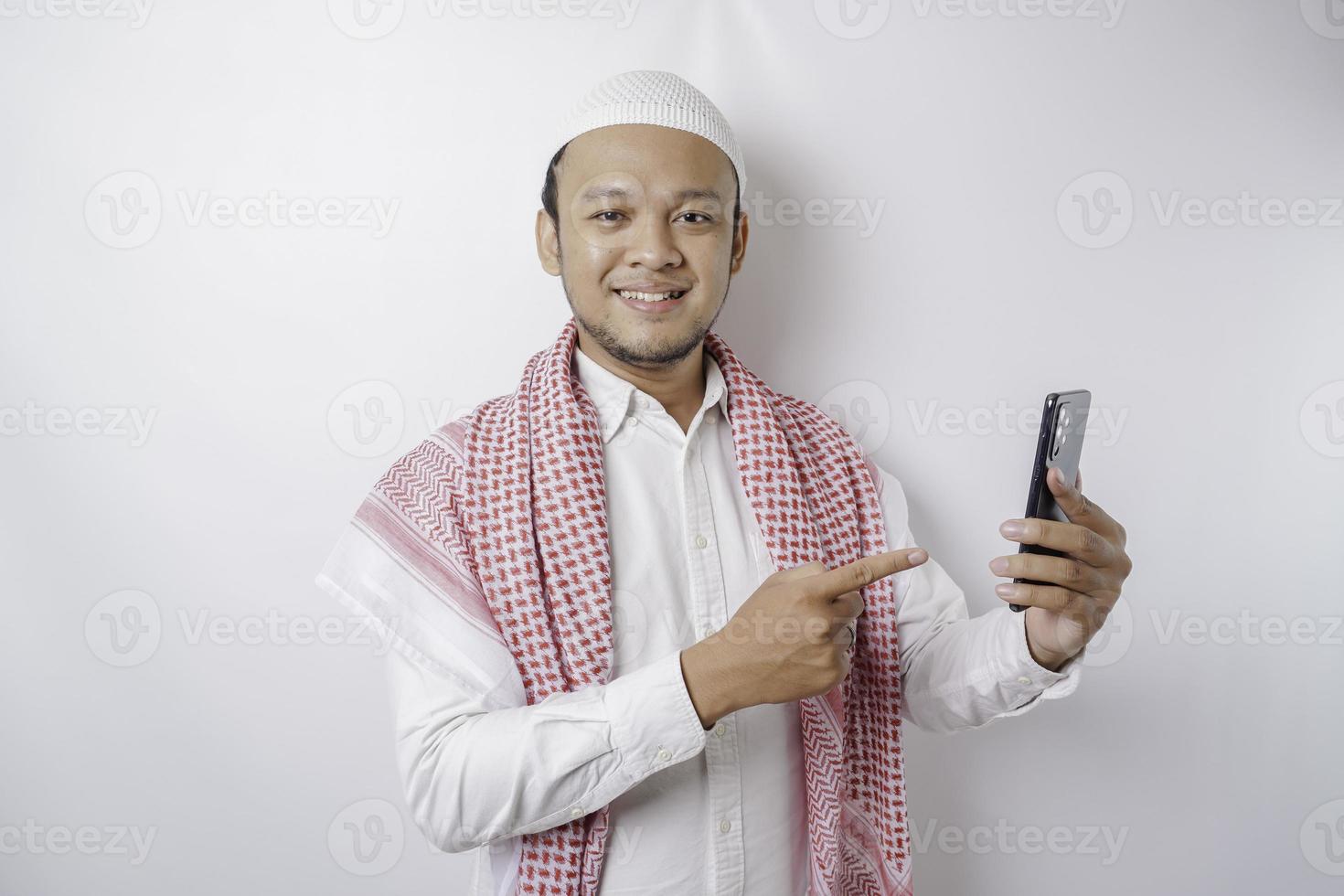 ein Porträt eines glücklichen asiatischen muslimischen Mannes, der lächelt, während er sein Telefon hält, isoliert durch weißen Hintergrund foto