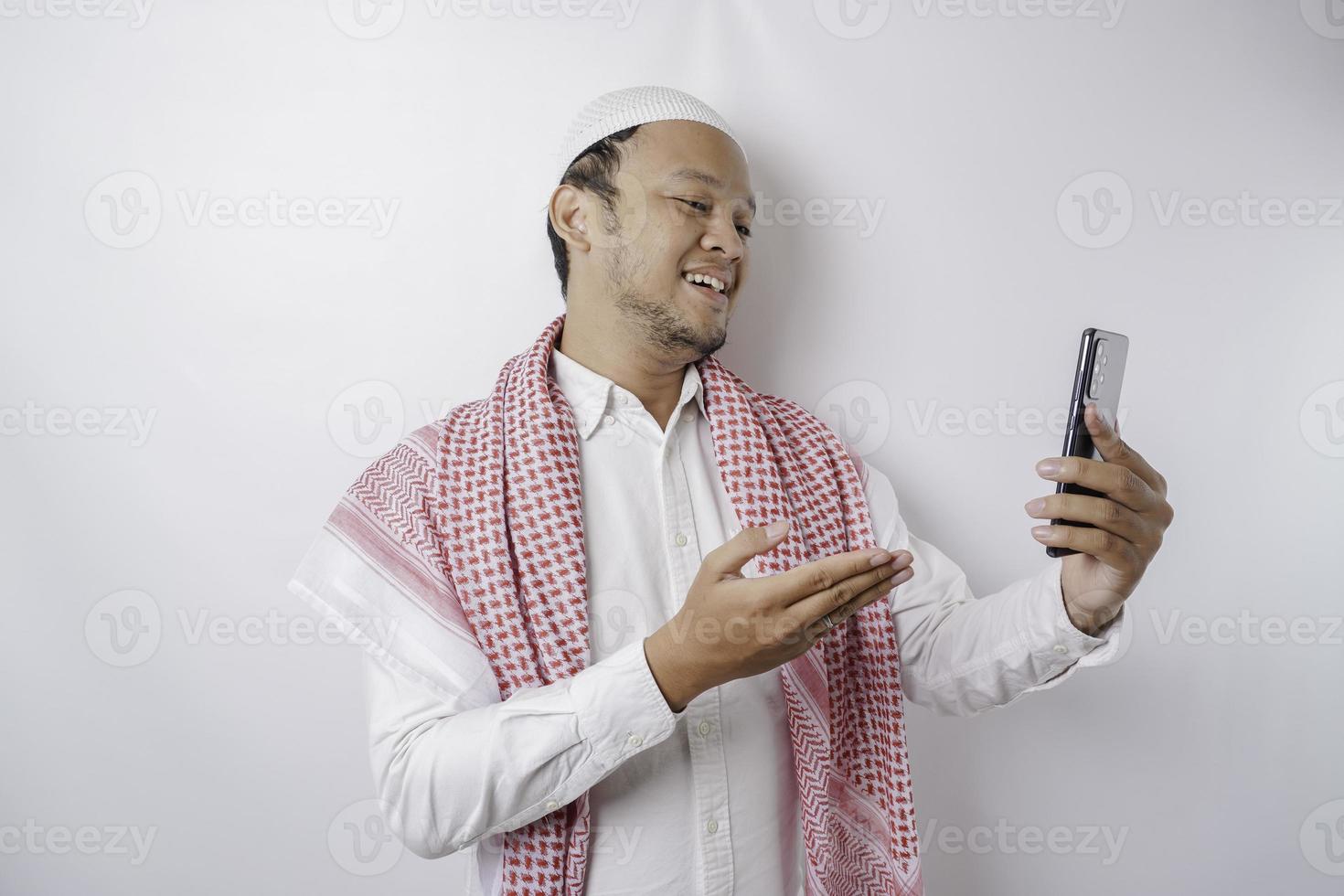 ein Porträt eines glücklichen asiatischen muslimischen Mannes, der lächelt, während er sein Telefon hält, isoliert durch weißen Hintergrund foto