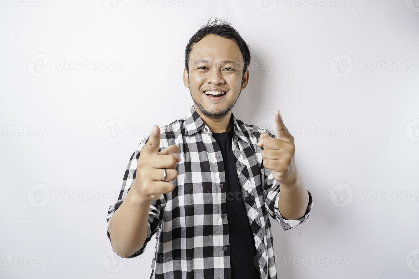 Junger asiatischer Mann mit Tartanhemd, der vor isoliertem weißem Hintergrund steht und mit glücklichem Gesicht mit dem Finger auf die Kamera zeigt. gute Energie und Stimmung. foto
