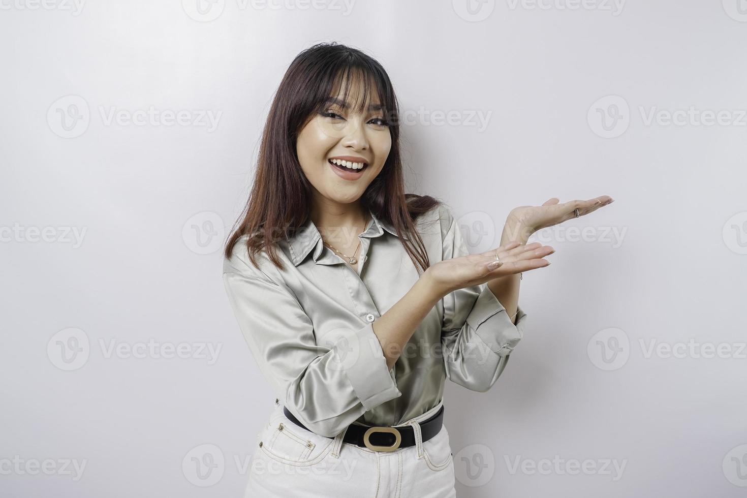 Aufgeregte asiatische Frau mit salbeigrünem Hemd, die auf den Kopierbereich neben ihr zeigt, isoliert durch weißen Hintergrund foto
