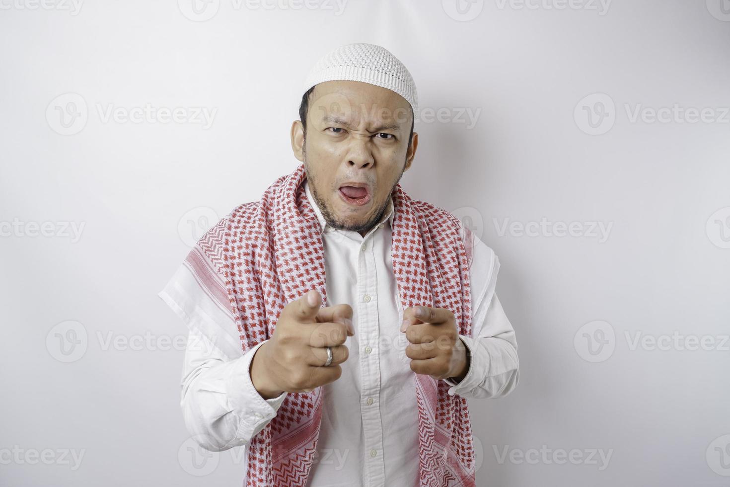 junger asiatischer muslimischer Mann, der vor isoliertem weißem Hintergrund steht und mit glücklichem Gesicht mit dem Finger auf die Kamera zeigt. gute Energie und Stimmung. foto