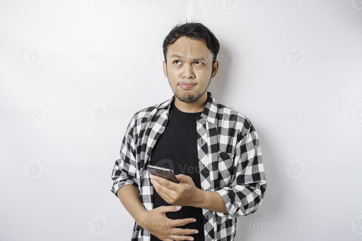 Foto eines hungrigen aufgeregten jungen Mannes, der sein Telefon hält und sich fragt, was er leckeres Essen einzeln auf weißem Farbhintergrund bestellen soll