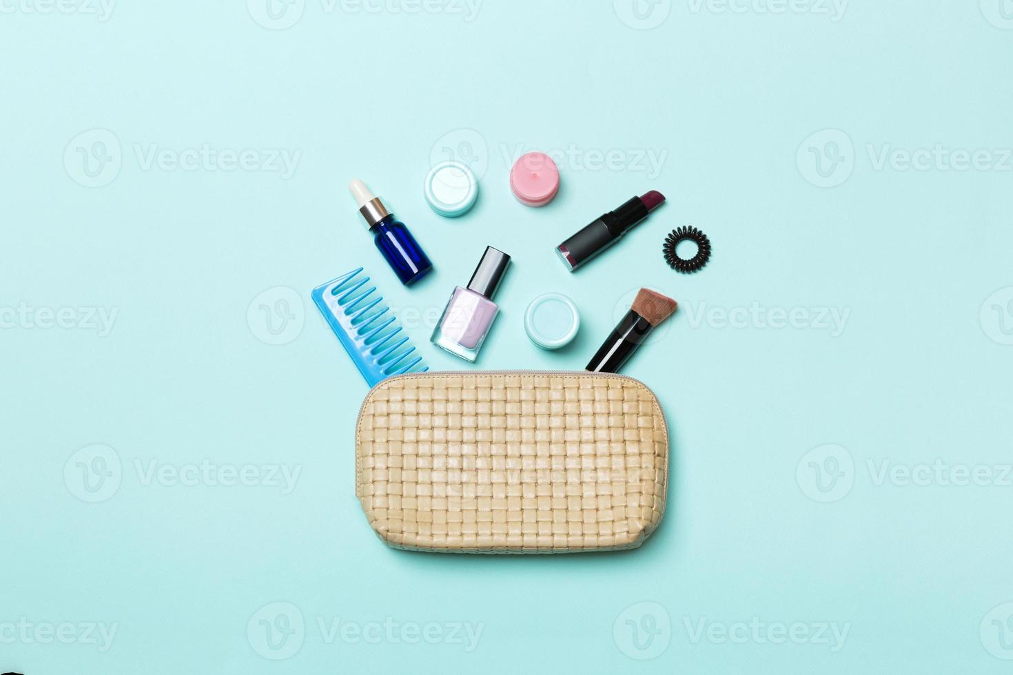 Draufsicht auf eine Reihe von Make-up- und Hautpflegeprodukten, die aus der Kosmetiktasche auf blauem Hintergrund verschüttet werden. Beauty-Konzept foto