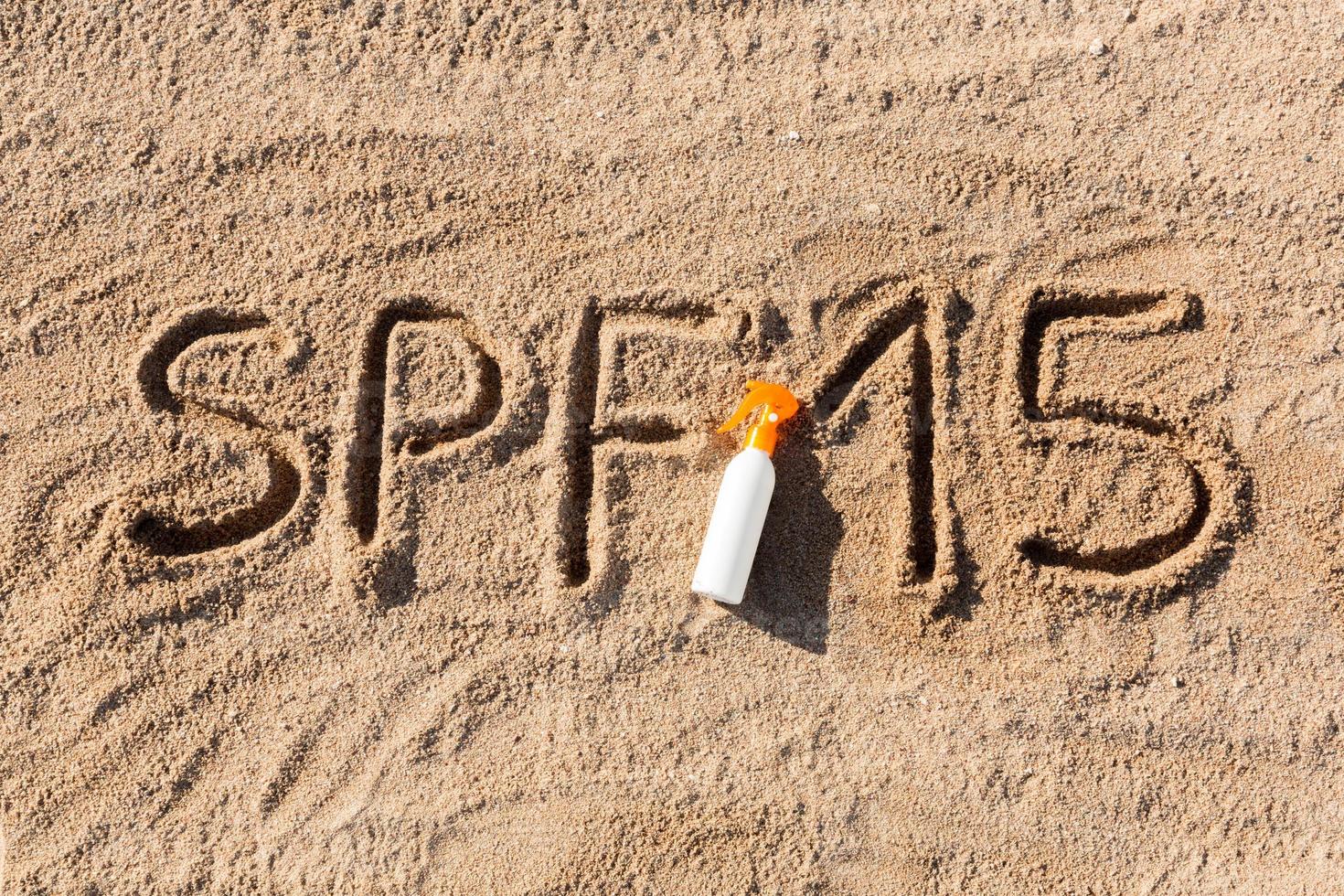 Sonnenschutzfaktor fünfzehn. spf 15 wort geschrieben auf dem sand und der weißen flasche mit sonnencreme. hintergrund des hautpflegekonzepts foto