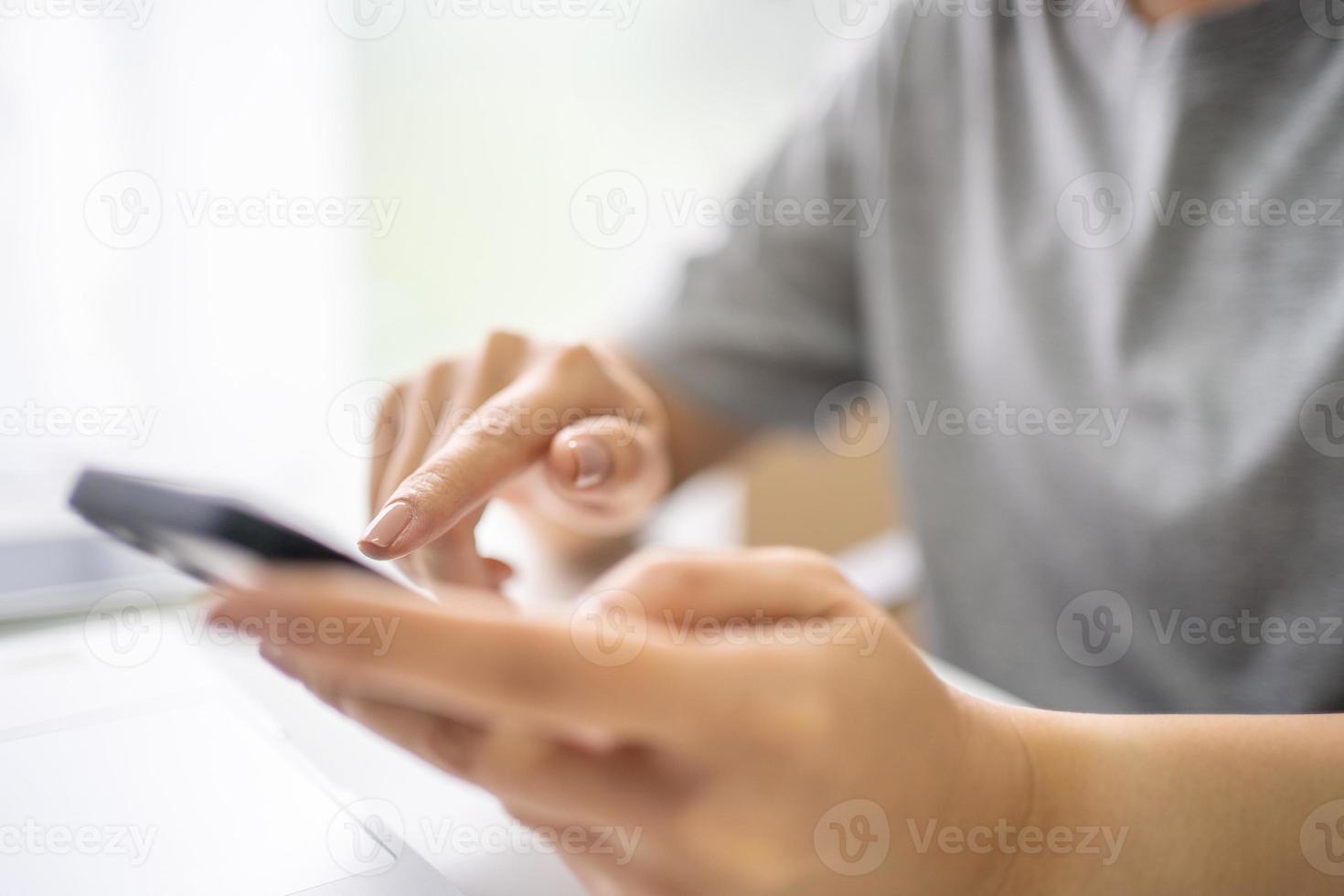 Nahaufnahme einer Frau, die ein Mobiltelefon in ihren Händen hält und Textnachrichten sendet, während sie am Schreibtisch vor einem Laptop sitzt. foto