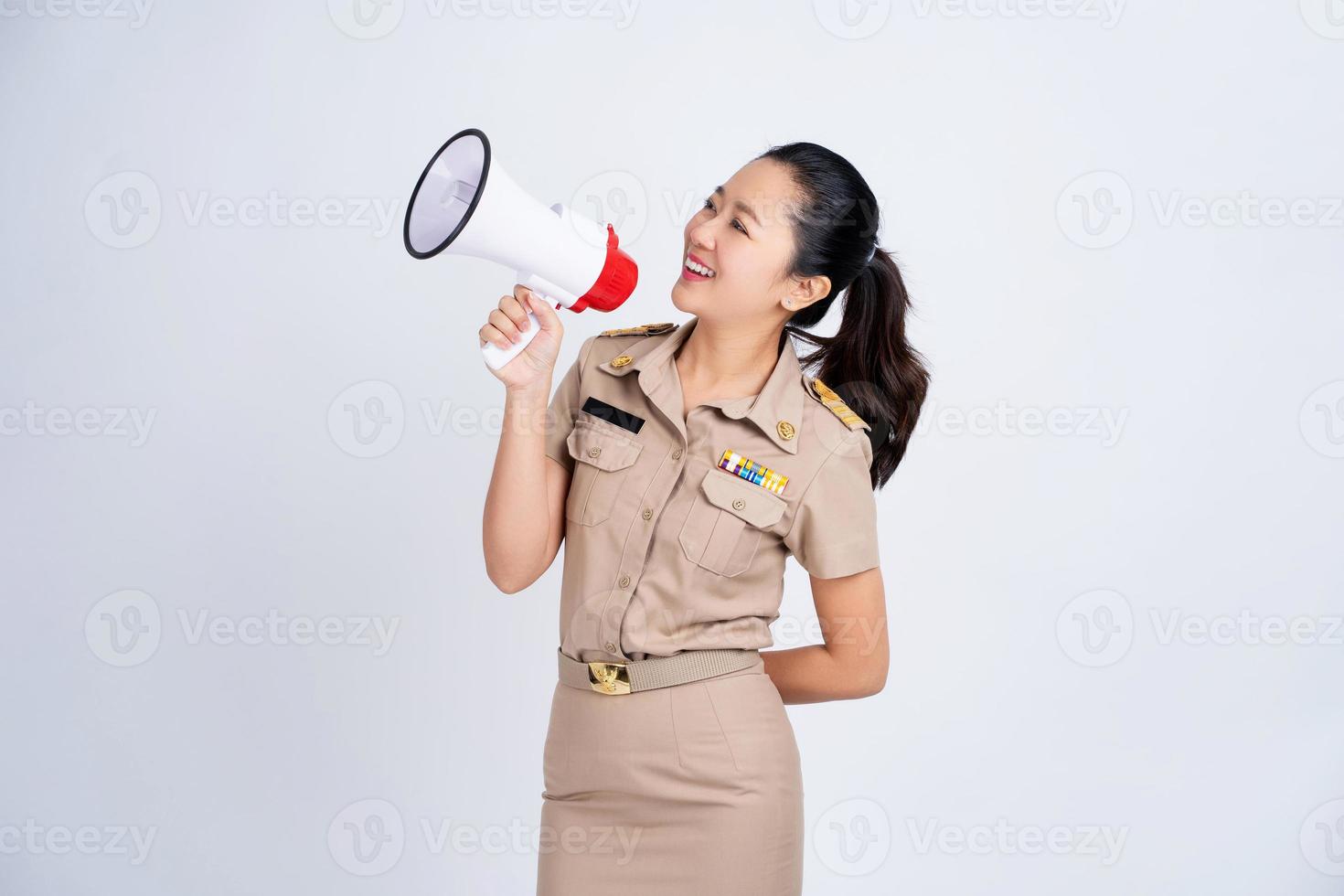 lächelnde junge asiatische Geschäftsfrau in brauner einheitlicher Arbeitskleidung. sie hält megaphon isoliert auf weißem hintergrund, lautsprecher und kündigt konzept an foto