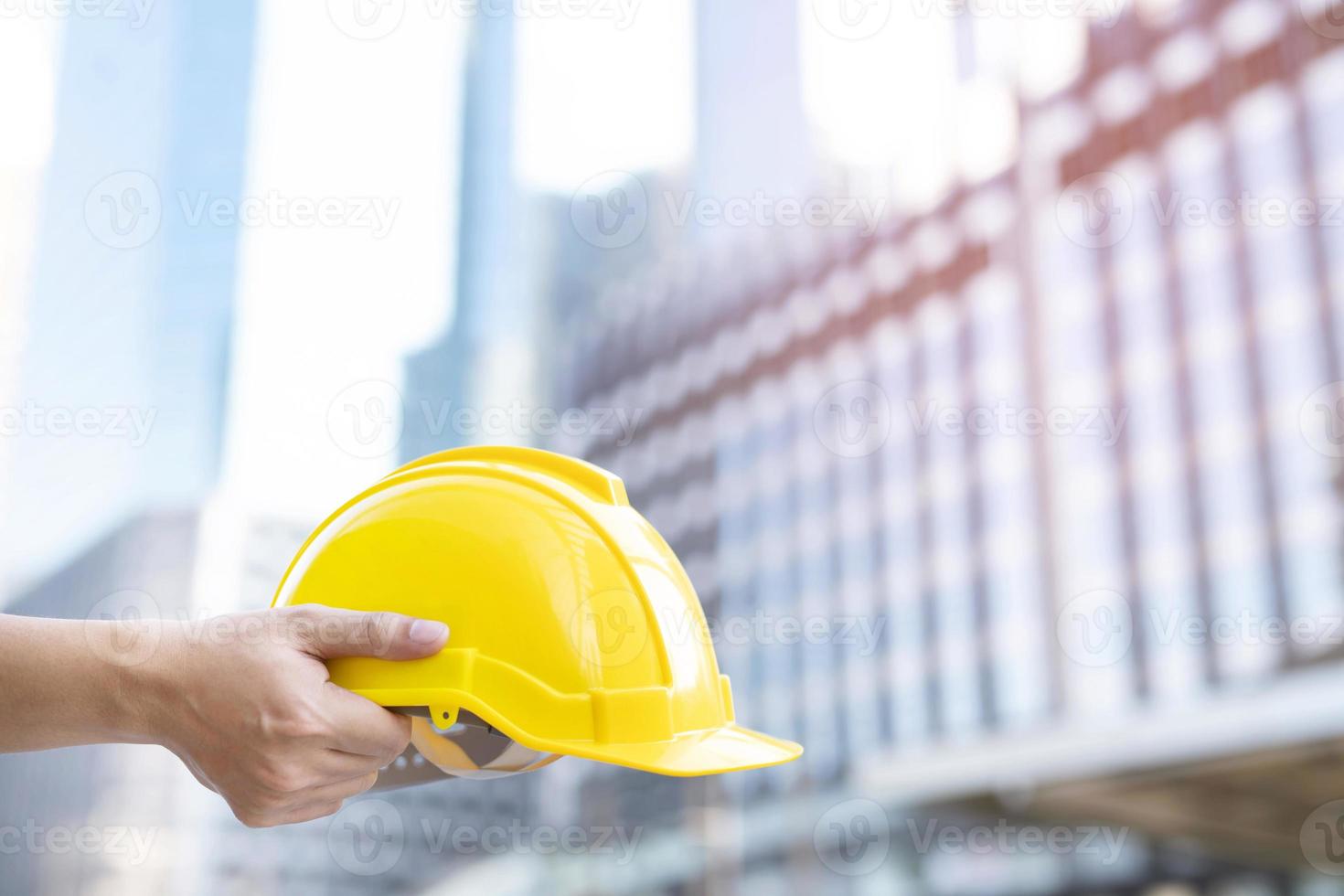 ein technischer männlicher bauarbeiter steht mit einem gelben sicherheitshelm und trägt reflektierende kleidung für die sicherheit des arbeitsbetriebs. im freien des gebäudehintergrundes. foto