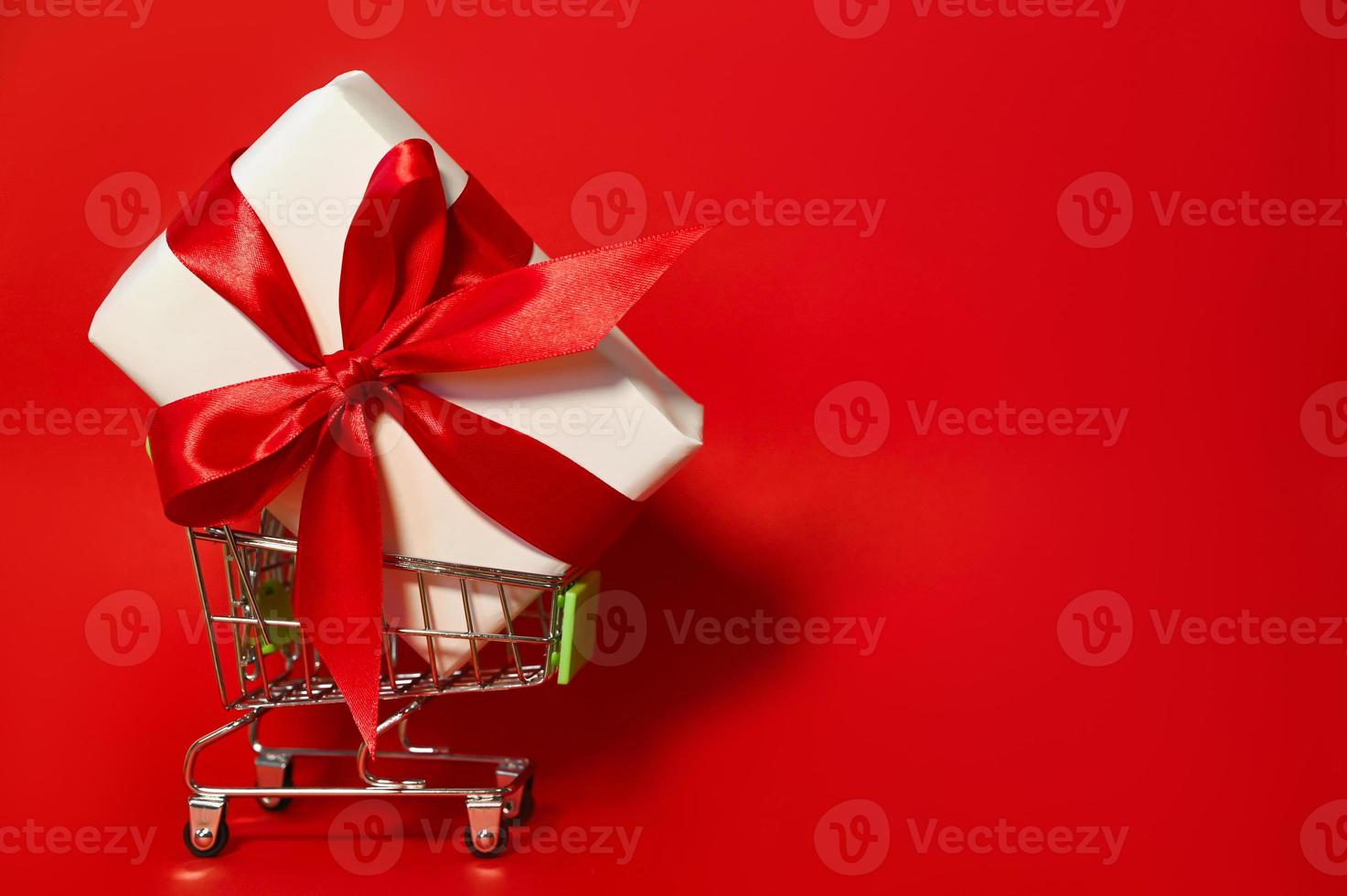 eine große Geschenkbox in einem Wagen vor rotem Hintergrund. Feiertage einkaufen und verkaufen. Rabatte. Attrappe, Lehrmodell, Simulation foto