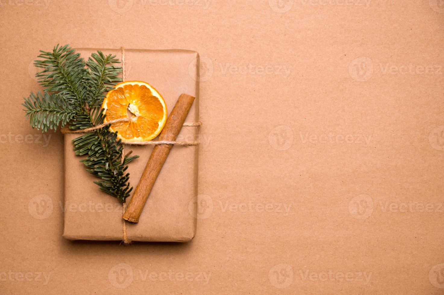 geschenk verpackt in recyceltem papier, verziert mit zimt, fichte und getrockneter orange, isoliert auf handwerklichem hintergrund. umweltfreundliches weihnachts- und neujahrskonzept. nachhaltiger lebensstil. modell, platz für text. foto