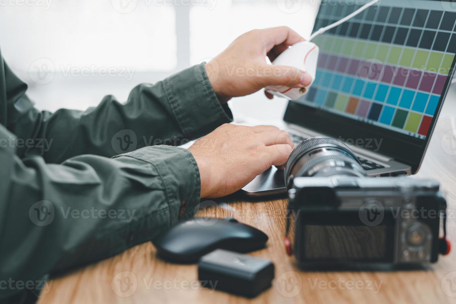 Nahaufnahme des Handfotografen, der auf der Laptoptastatur tippt, um das Programm in der Displaykalibrierung und den Kameraakku auf dem Holztisch anzupassen foto