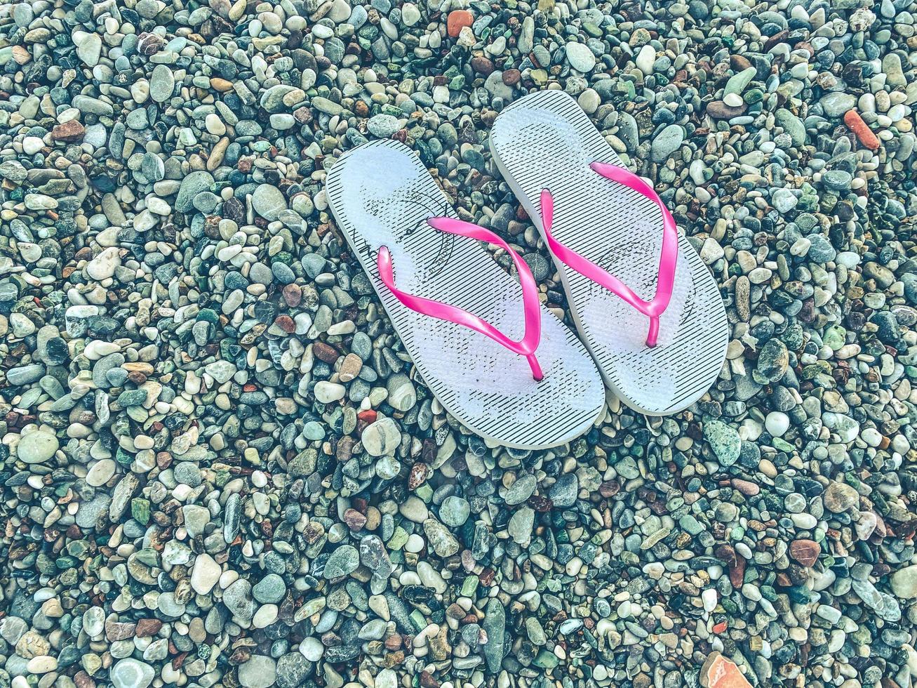 heißes, tropisches Land mit Meer und Bergen. Am Strand gibt es Kiesel und kleine Steine. auf dem boden liegen weiße damenpantoffeln zum spazieren foto