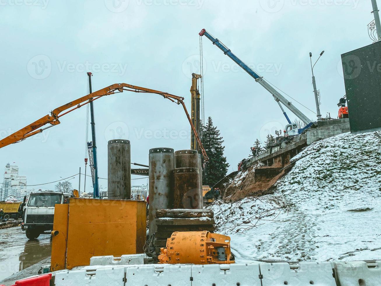 Bau einer neuen Brücke in der Innenstadt. Ausrüstung funktioniert im Winter im Schnee. Ein schwerer Großkran trägt Betonkonstruktionen für den Bau einer Überführung foto