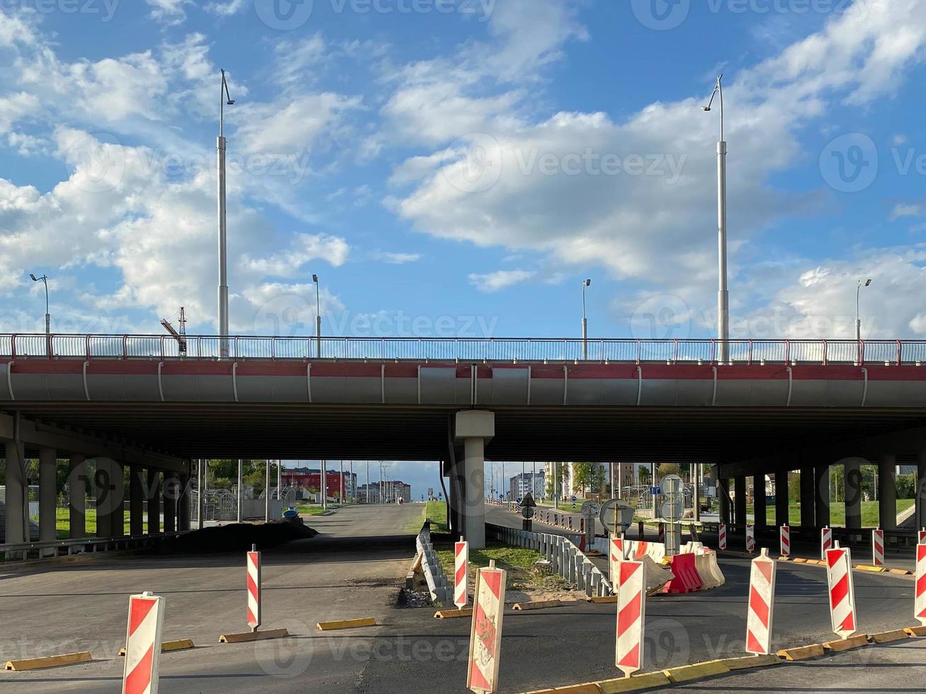 reparatur und bau einer straße mit provisorischen verkehrszeichen und kegeln auf dem hintergrund einer großen autobahnbrücke in einer großstadt foto