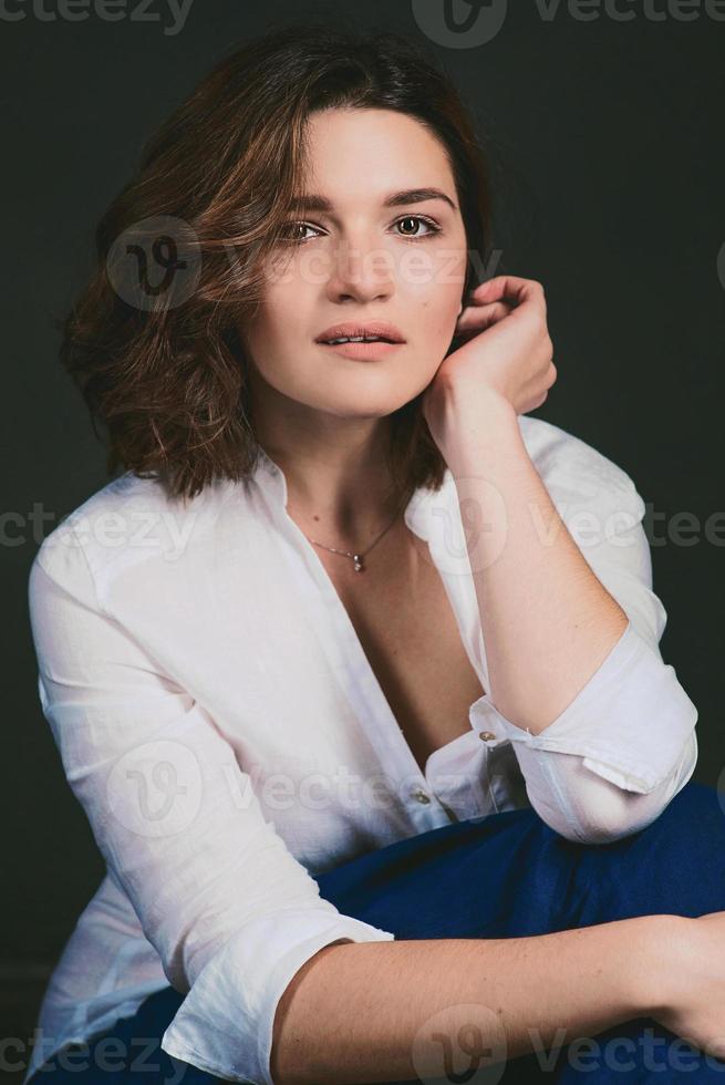 Porträt einer jungen, schönen traurigen Schauspielerin mit kurzen braunen Haaren in weißem Hemd und blauer Hose im Studio foto