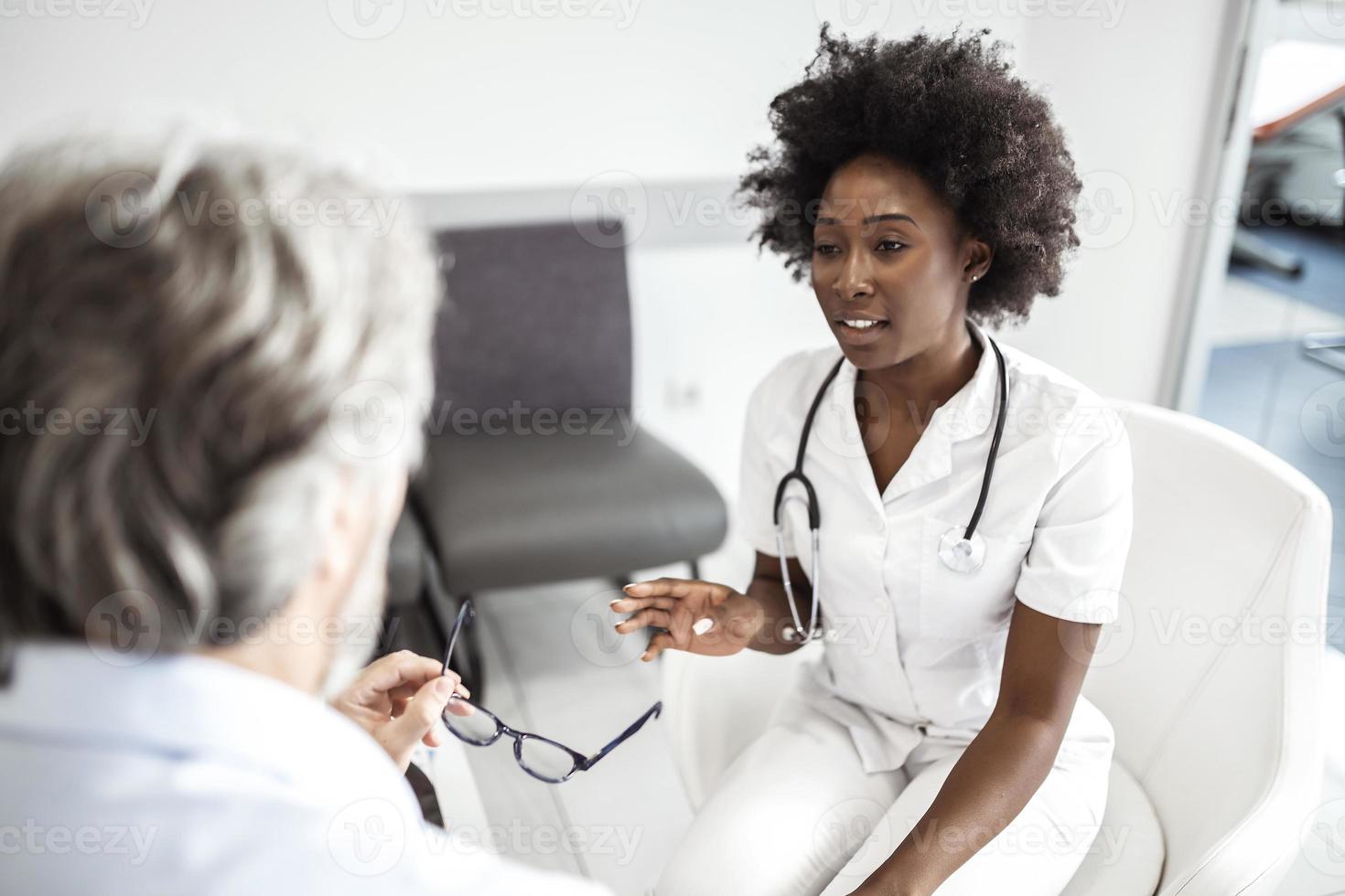 afroamerikanische ärztin, die ihre reife patientin im wartezimmer einer medizinischen klinik tröstet. foto