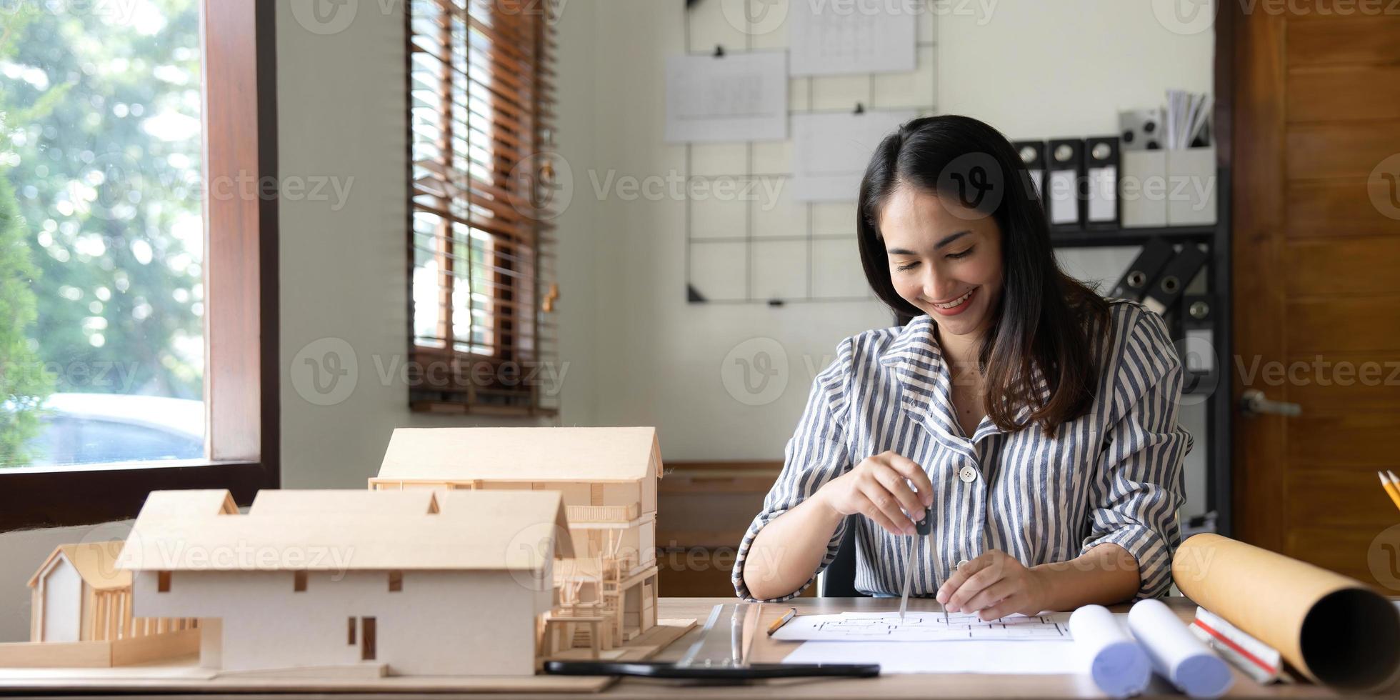 Architektur-, Bau-, Konstruktions- und Immobilienkonzept - glücklich lächelnde Architektin mit Bauplan, Lineal und Wohnhausmodell auf dem Tisch, der im Heimbüro arbeitet. Architektin Frau. foto