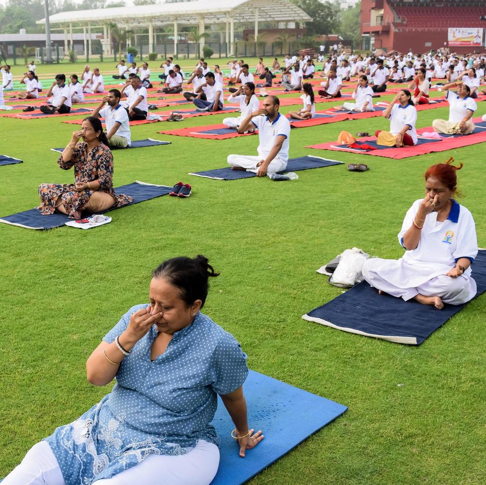 neu-delhi, indien, 21. juni 2022 - gruppen-yoga-übungssitzung für menschen im yamuna-sportkomplex in delhi am internationalen yoga-tag, große gruppe von erwachsenen, die an yoga-kursen im cricket-stadion teilnehmen foto